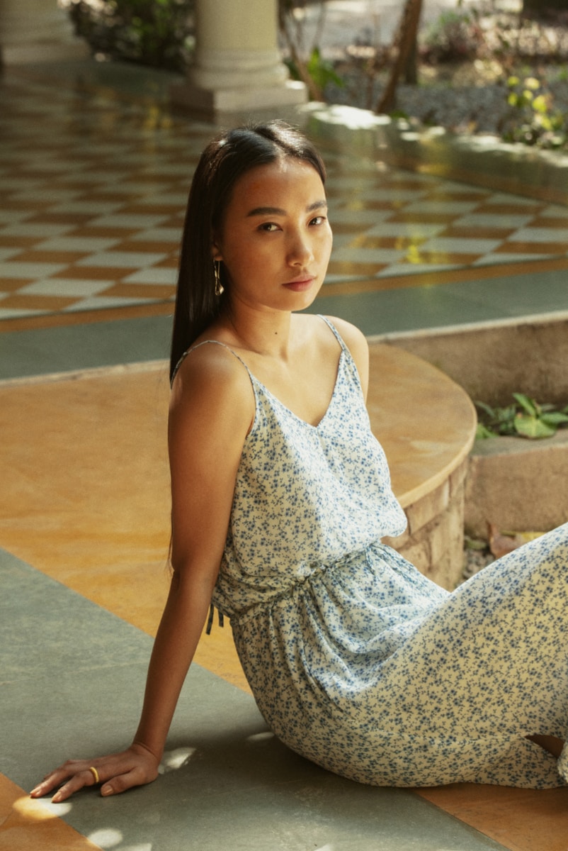 A young woman in a floral jumpsuit sits outdoors.