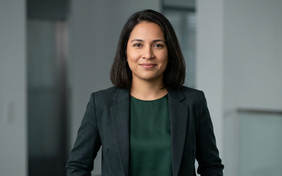 Photorealistic portrait of a confident woman in a tailored dark blazer and green blouse, smiling, against a neutral blurred background.